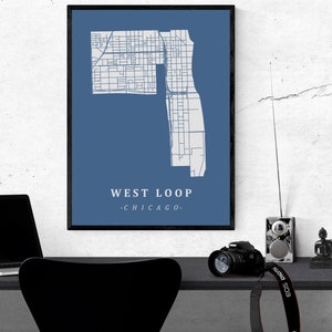 May include: A framed print featuring a map of the West Loop neighborhood in Chicago, Illinois. The map is in white against a blue background, with the text "WEST LOOP - CHICAGO" in white. The print is in a black frame.
