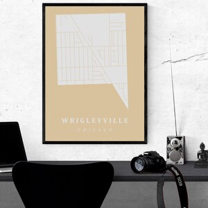 May include: A framed map print of the Wrigleyville neighborhood in Chicago. The map is in a minimalist style with a light gray design on a tan background. The text "Wrigleyville Chicago" is at the bottom.