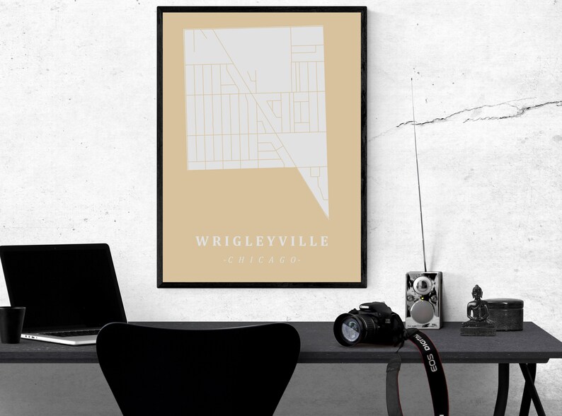 May include: A framed map print of the Wrigleyville neighborhood in Chicago. The map is in a minimalist style with a light gray design on a tan background. The text "Wrigleyville Chicago" is at the bottom.