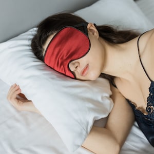 May include: A person sleeping on a white pillow with a red sleep mask over their eyes.