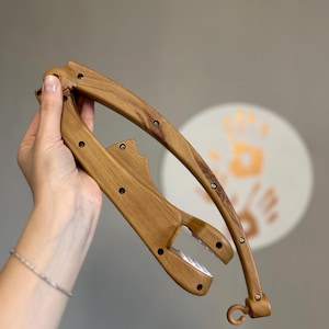 Puede incluir: Un brazo de móvil para bebé de madera, con forma curva y un gancho en el extremo. El brazo está hecho de madera marrón claro con un acabado natural. Tiene varios agujeros pequeños perforados.