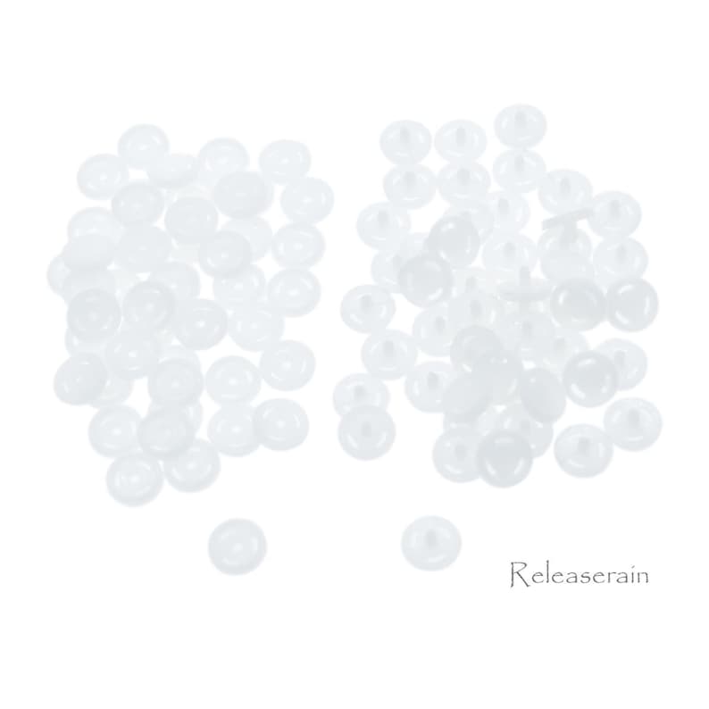 May include: A large quantity of white plastic buttons, ideal for crafts and sewing projects. The buttons are round with a small raised center and a flat back.