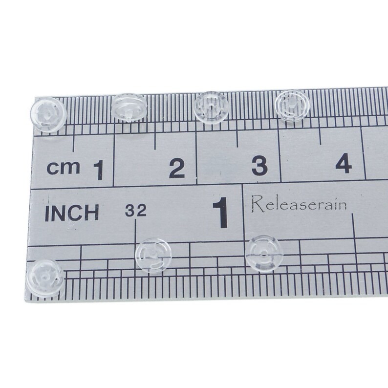 May include: Close-up of clear plastic buttons, measuring approximately 1/2 inch in diameter, against a ruler marked in inches and centimeters.