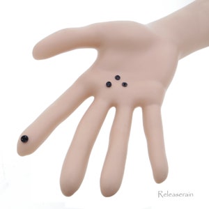May include: Four small black screws on a hand, with one screw on a finger.