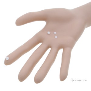 May include: Four small white plastic buttons, three are on a hand and one is on a finger.