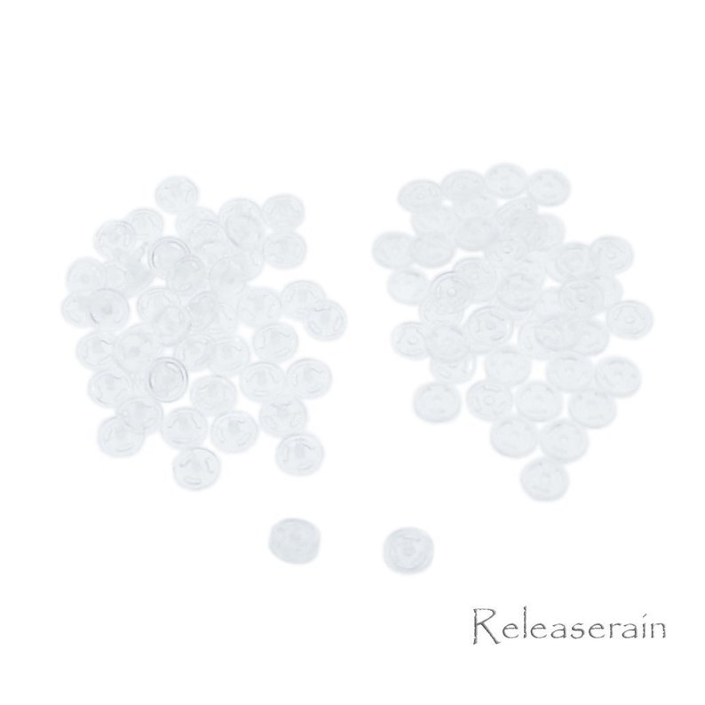 May include: A large pile of clear plastic buttons, with a smaller pile of buttons to the right. The buttons are all the same size and shape, and they are arranged in a random pattern.