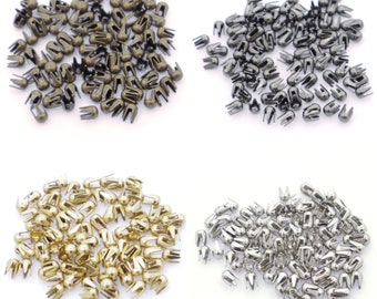 May include: Four piles of metal rivets in different colors: gold, bronze, black, and silver. The rivets are small and have a rounded head with two prongs.
