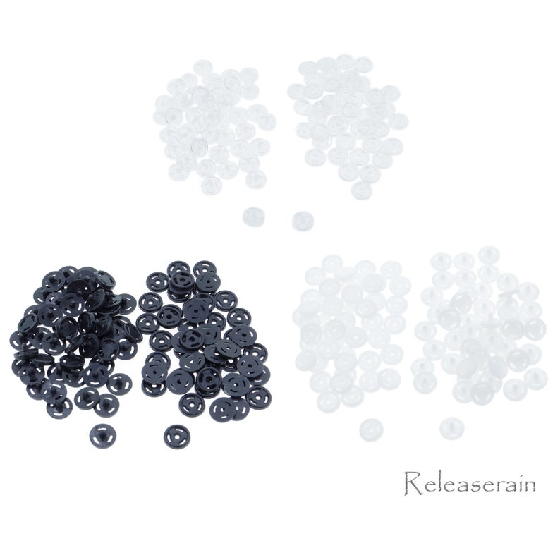 May include: A pile of black plastic snap buttons and two piles of clear plastic snap buttons.