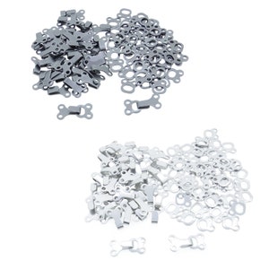 Può includere: Due pile di chiusure per indumenti in metallo argentato. Una pila contiene 50 anelli di metallo e l'altra pila contiene 50 ganci di metallo. Ci sono anche tre ganci di metallo singoli.