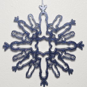 May include: A blue glitter snowflake ornament with a star-shaped top. The snowflake is made of a thin, clear material and has a delicate design.
