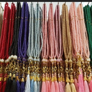 May include: A collection of colorful prayer beads with gold tassels. The beads are made of various materials, including pearls and glass. The tassels are adorned with gold charms.
