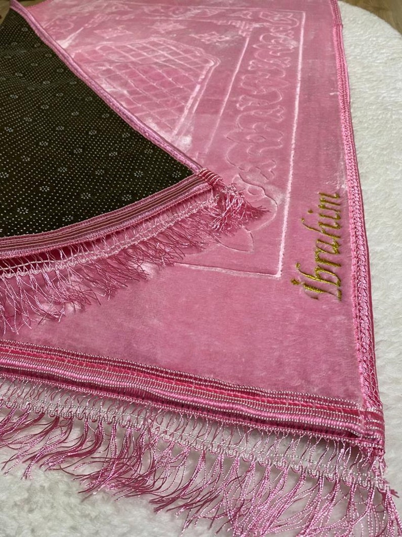 May include: Pink prayer rug with gold embroidery and fringe. The rug has a non-slip backing and is made of soft, plush fabric.