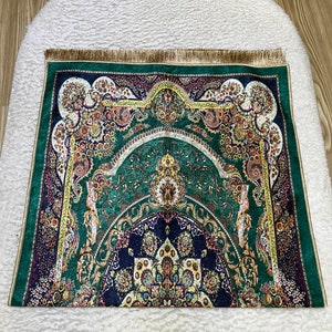 Peut inclure: Un tapis de pri&egrave;re vert avec des motifs floraux et g&eacute;om&eacute;triques complexes dans des tons d'or, de bleu et de rouge. Le tapis a une bordure de franges dor&eacute;es.