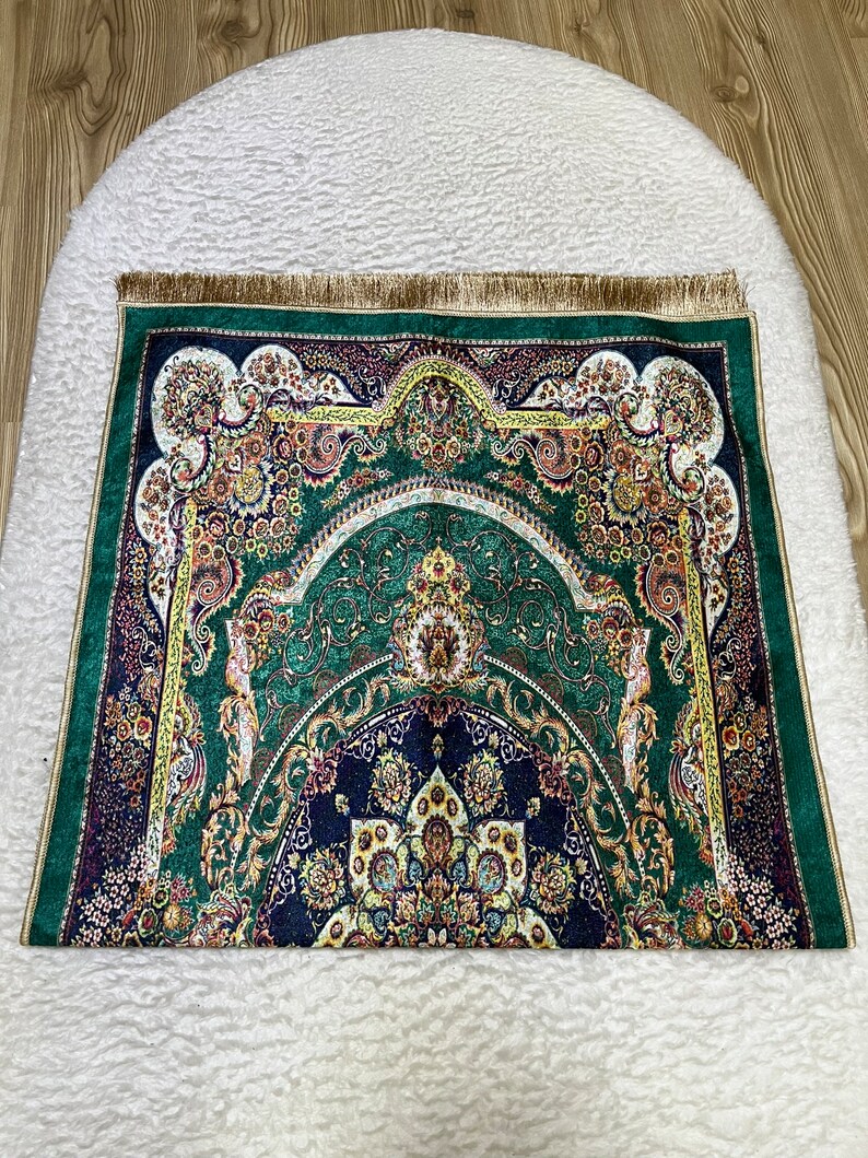 Peut inclure: Un tapis de pri&egrave;re vert avec des motifs floraux et g&eacute;om&eacute;triques complexes dans des tons d'or, de bleu et de rouge. Le tapis a une bordure de franges dor&eacute;es.