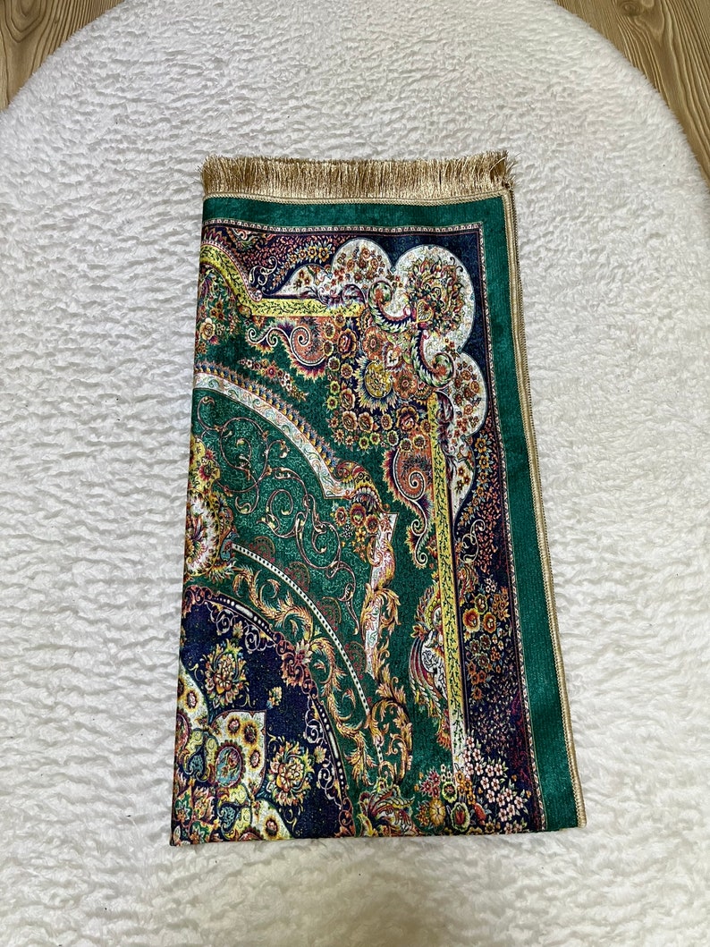 Peut inclure: Un tapis de pri&egrave;re vert et or avec un motif persan traditionnel. Le tapis a une bordure &agrave; franges et est fait d'un tissu doux et luxueux.