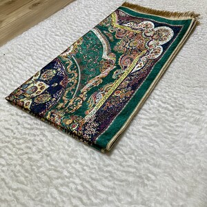 Peut inclure: Un tapis de pri&egrave;re vert avec une frange dor&eacute;e et des motifs floraux complexes dans des tons de bleu, jaune et rouge.