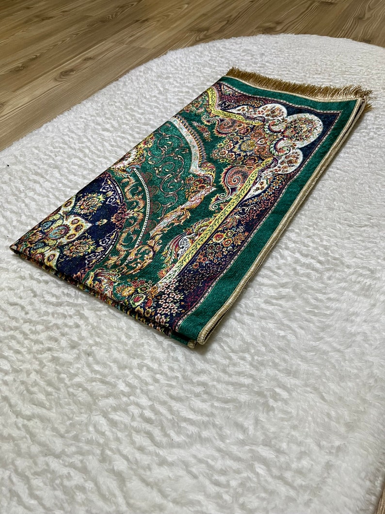 Peut inclure: Un tapis de pri&egrave;re vert avec une frange dor&eacute;e et des motifs floraux complexes dans des tons de bleu, jaune et rouge.