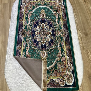 Peut inclure: Un tapis de pri&egrave;re vert avec des motifs floraux et dor&eacute;s complexes. Le tapis a une bordure frang&eacute;e et un dos antid&eacute;rapant.