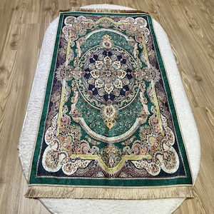 Peut inclure: Un tapis vert, or et brun &agrave; motifs avec une bordure frang&eacute;e. Le tapis a un m&eacute;daillon central avec des motifs floraux complexes.