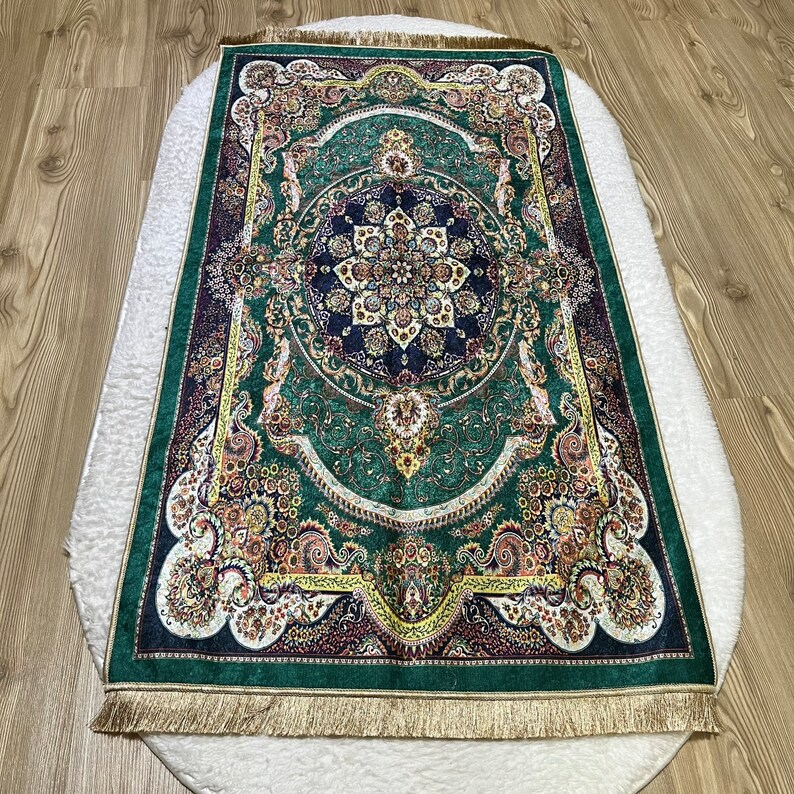 Peut inclure: Un tapis vert, or et brun &agrave; motifs avec une bordure frang&eacute;e. Le tapis a un m&eacute;daillon central avec des motifs floraux complexes.