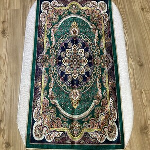 Peut inclure: Un tapis de pri&egrave;re vert avec un motif floral dor&eacute; et bleu et une bordure en frange dor&eacute;e.