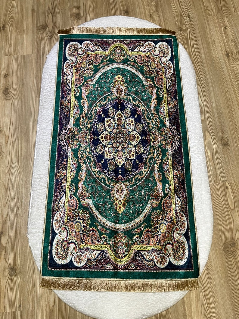 Peut inclure: Un tapis de pri&egrave;re vert avec un motif floral dor&eacute; et bleu et une bordure en frange dor&eacute;e.