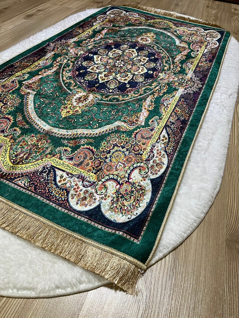 Peut inclure: Un tapis de pri&egrave;re vert avec une frange dor&eacute;e et des motifs floraux complexes. Le tapis a un m&eacute;daillon central avec un motif bleu et or.