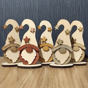 May include: Five wooden gnomes with white hats and brown, red, yellow, blue, and grey painted details. Each gnome has a star on its hat and a white beard.
