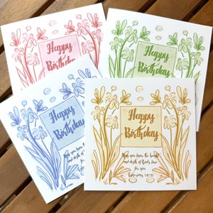 Könnte beinhalten: Vier handgefertigte Grußkarten mit Blumendesigns und dem Text "Happy Birthday". Jede Karte hat ein anderes Farbschema: rosa, grün, blau und gelb. Die Karten enthalten auch einen Bibelvers über Gottes Liebe.