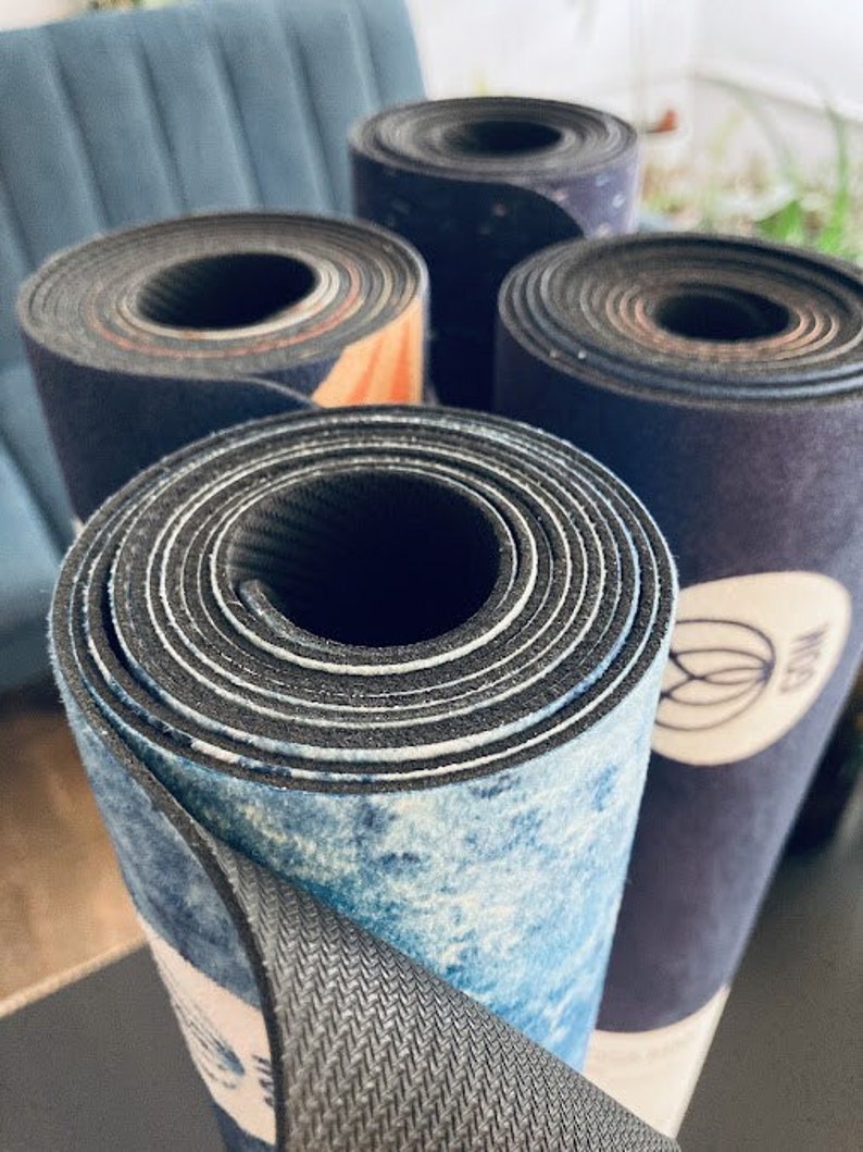 May include: Close-up of four rolled-up yoga mats with different patterns. The mats are made of a textured material and have a variety of colors, including blue, black, and white.