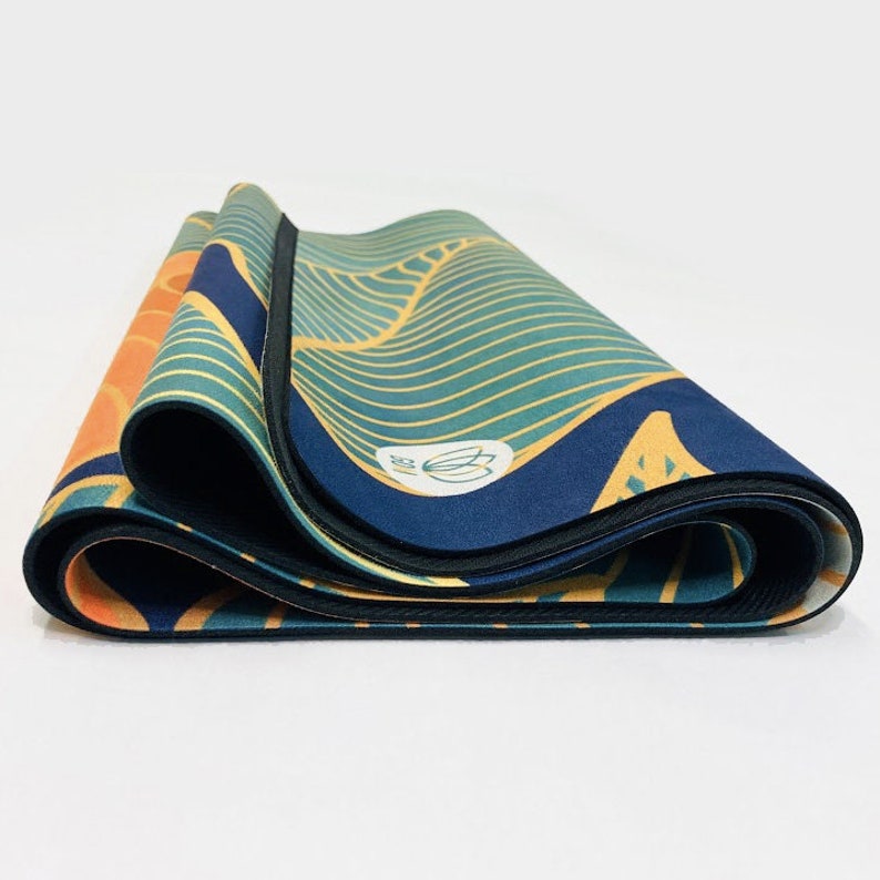 May include: A folded yoga mat with a blue, green, and orange geometric pattern. The mat has a black border and a small white logo with a lotus flower.