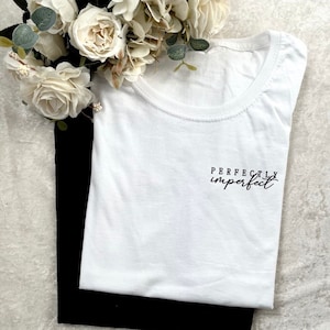 Könnte beinhalten: Weißes T-Shirt mit dem Text "Perfectly imperfect" in schwarzer, kursiv geschriebener Schrift.