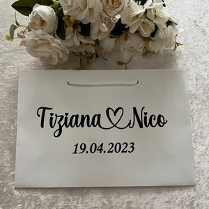 Puede incluir: Bolsa de regalo blanca con texto negro que dice "Tiziana Nico" con un s&iacute;mbolo de coraz&oacute;n y la fecha "19.04.2023".