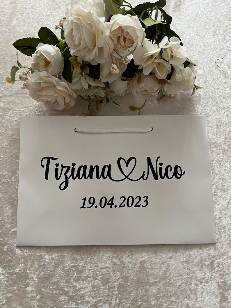 Puede incluir: Bolsa de regalo blanca con texto negro que dice "Tiziana Nico" con un s&iacute;mbolo de coraz&oacute;n y la fecha "19.04.2023".