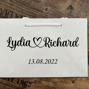 Puede incluir: Bolsa de regalo blanca con texto negro que dice "Lydia &hearts; Richard" y "13.08.2022".