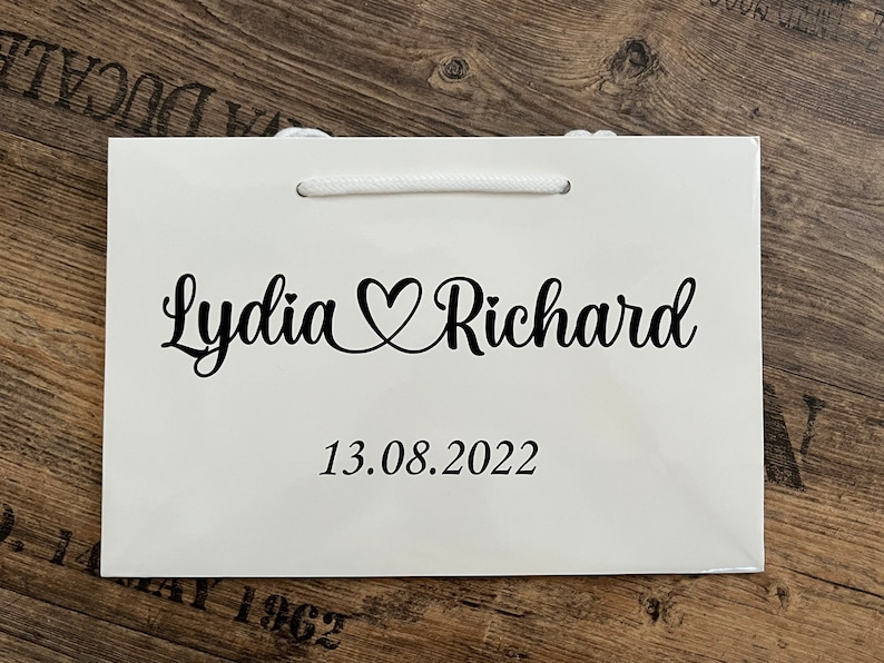 Puede incluir: Bolsa de regalo blanca con texto negro que dice "Lydia &hearts; Richard" y "13.08.2022".