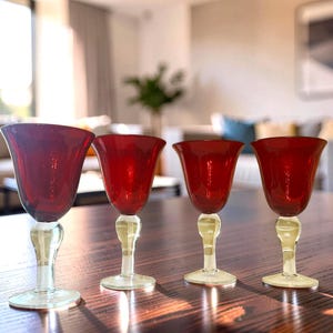 Puede incluir: Un conjunto de cuatro copas con cáliz de color rojo intenso y tallo y base de cristal transparente. Cada copa presenta un borde ancho y acampanado, además de una sección redondeada y bulbosa en el tallo, manteniendo un diseño uniforme.