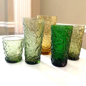 May include: A selection of vintage textured drinking glasses in shades of green and amber. The set includes tall and short glasses, with a unique, organic pattern. Ideal for serving drinks.
