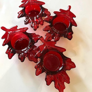 May include: Set of three red glass candle holders shaped like oak leaves. Each holder has a small, round opening for a tea light candle.