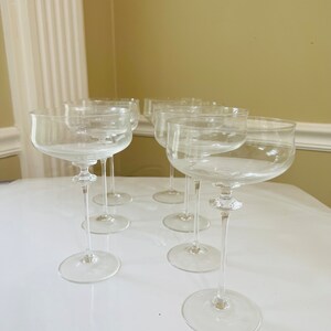 May include: Set of six clear glass champagne coupes with a wide bowl and a long, thin stem.