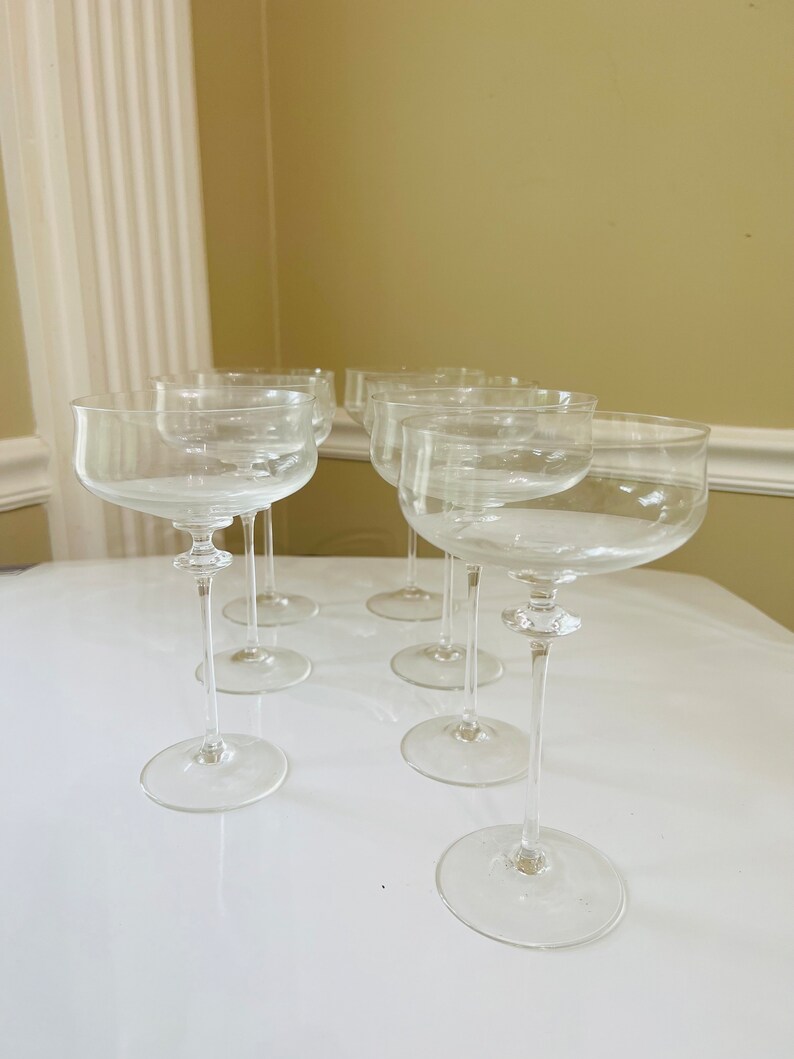 May include: Set of six clear glass champagne coupes with a wide bowl and a long, thin stem.