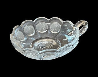 May include: A clear glass bowl with a scalloped edge and a handle. The bowl is decorated with a repeating pattern of coins.