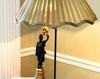 May include: A table lamp with a pleated green lampshade and a black and gold base featuring a figurine of a person holding a lantern.
