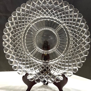 May include: A clear glass serving plate with a diamond pattern and a divided center section. The plate is on a wooden stand.