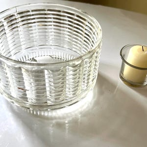 May include: A clear glass candle holder with a ribbed design and a smaller clear glass candle holder with a white candle inside.