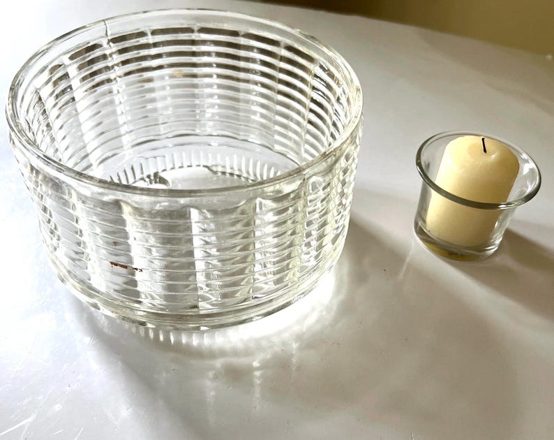 May include: A clear glass candle holder with a ribbed design and a smaller clear glass candle holder with a white candle inside.