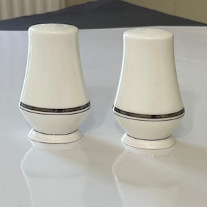 May include: Two white ceramic salt and pepper shakers with a gold band around the middle.