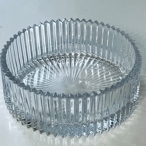 Puede incluir: Un cuenco de vidrio transparente con un diseño acanalado. El cuenco tiene una forma circular y una base ancha y poco profunda.