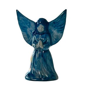 May include: A blue ceramic angel figurine with wings outstretched and hands clasped in prayer. The angel is kneeling and has a white face.
