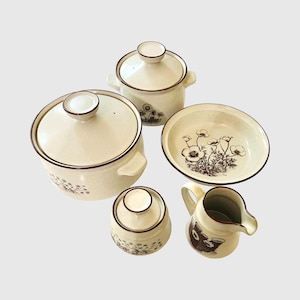 Könnte beinhalten: Ein cremefarbenes Keramikgeschirr-Set mit floralem Design. Das Set umfasst einen großen Topf mit Deckel, einen kleineren Topf mit Deckel, eine Schüssel, einen Sahnekännchen und eine Zuckerdose. Jedes Teil hat einen braunen Rand und ein Blumenmuster.
